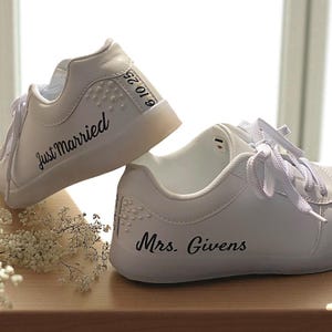 May include: White sneakers with laces, featuring the text "Just Married" and "Mrs. Givens" in black script. The date "6.10.25" is also visible. These shoes are a perfect wedding accessory.