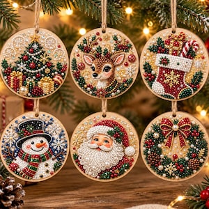 May include: A set of six circular wooden Christmas ornaments featuring diamond art designs of a decorated tree, a reindeer, a stocking, a snowman, Santa Claus, and a wreath, each hanging from a jute twine loop with colourful bead accents.