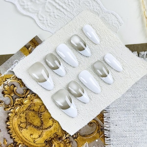Könnte beinhalten: Ein Set aus weißen und grauen Ombre-Press-On-Nägeln. Die Nägel sind oval geformt und haben eine weiße Basis und ein graues Ombre-Design an den Spitzen. Sie sind auf einer strukturierten weißen Oberfläche angeordnet.
