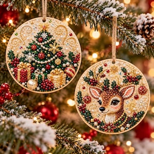May include: Two round, flat Christmas ornaments featuring intricate beadwork. One displays a decorated pine tree with gifts, while the other shows a deer head surrounded by holly, berries, and snowflakes. Both hang from jute twine loops.