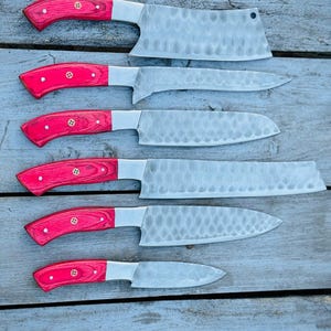 Puede incluir: Un juego de seis cuchillos de cocina con mangos de madera roja y hojas plateadas. Las hojas tienen un aspecto texturizado y martillado. Los cuchillos var&iacute;an en tama&ntilde;o y forma, incluyendo una cuchilla y un cuchillo peque&ntilde;o. Los mangos est&aacute;n asegurados con remaches de lat&oacute;n.