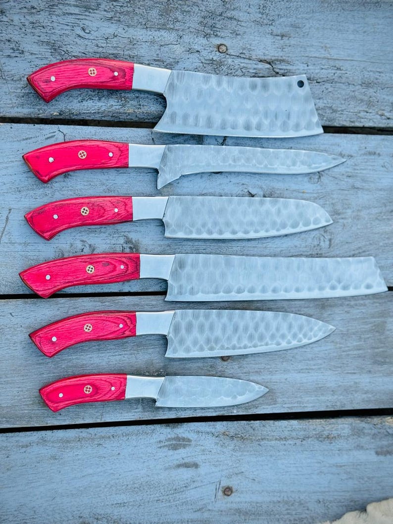 Puede incluir: Un juego de seis cuchillos de cocina con mangos de madera roja y hojas plateadas. Las hojas tienen un aspecto texturizado y martillado. Los cuchillos var&iacute;an en tama&ntilde;o y forma, incluyendo una cuchilla y un cuchillo peque&ntilde;o. Los mangos est&aacute;n asegurados con remaches de lat&oacute;n.