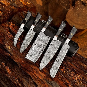 以下が含まれることがあります： 黒い柄と革製の鞘が付いた、ダマスカス鋼のナイフ6本セット。 刃には独特の渦巻き模様があります。 ナイフは素朴な木製の表面に展示されており、その職人技とデザインが際立っています。