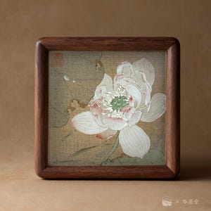 May include: A framed artwork featuring a detailed illustration of a white lotus flower with pink accents and a green center. The artwork is set against a beige background and encased in a dark brown wooden frame. The frame has rounded corners.