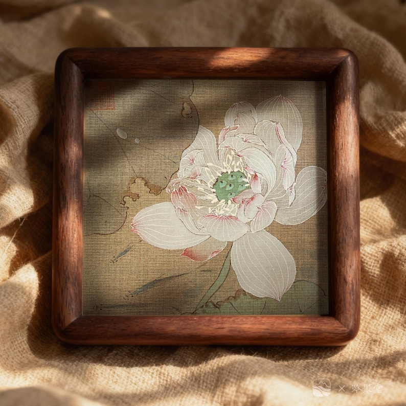 May include: Square wooden frame with a detailed illustration of a white lotus flower with pink accents and a green center. The artwork is set against a muted green and tan background, framed by a rich, dark brown wood.