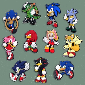 May include: A collection of colorful cartoon character charms, featuring Sonic the Hedgehog and other characters. The charms are in various poses and colors, including blue, red, green, and yellow. These charms are likely for shoes or accessories.