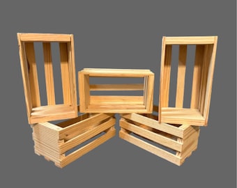 May include: Five unfinished wooden crates of varying sizes are arranged against a gray background. The crates are rectangular with slatted sides and are made of light-colored wood. The crates are empty and appear to be new.