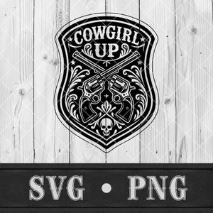May include: Black and white graphic design featuring the text "COWGIRL UP" within a shield shape. Two crossed revolvers are centered, with floral and skull accents. The bottom banner reads "SVG • PNG".
