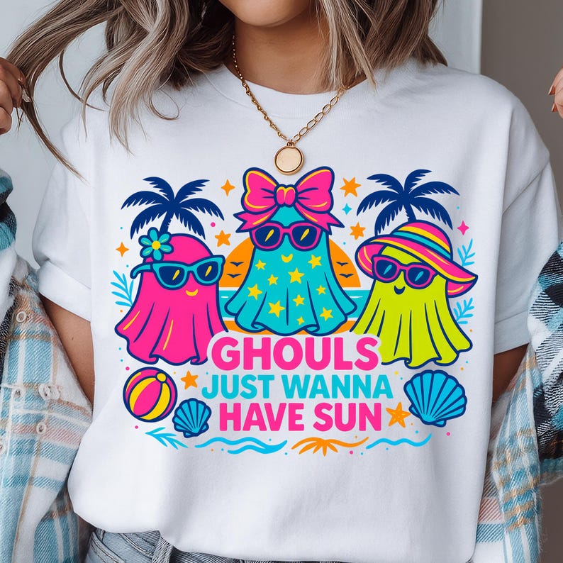 May include: White t-shirt featuring a colorful graphic of three cartoon ghosts wearing sunglasses and beach attire. The text "GHOULS JUST WANNA HAVE SUN" is printed below the ghosts, with beach-themed illustrations.