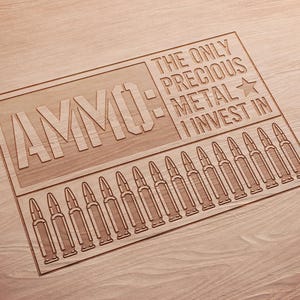 May include: Wooden sign with the word "AMMO" and the phrase "THE ONLY PRECIOUS METAL I INVEST IN" engraved. Below the text are engraved bullet casings. The sign is made of light brown wood.
