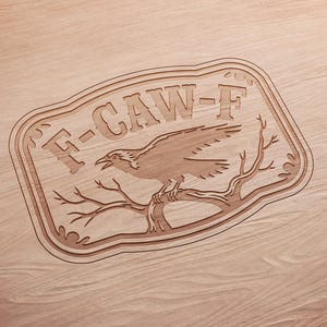 May include: A wooden sign with the text "F-CAW-F" and a detailed carving of a raven perched on a branch. The sign has a decorative border and is set against a wood grain background.
