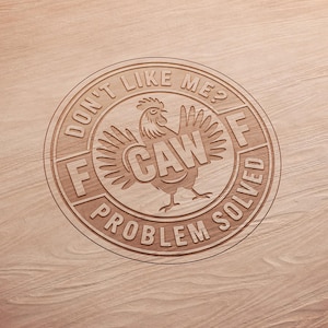 May include: A wooden circle with the text "DON'T LIKE ME? F CAW PROBLEM SOLVED" engraved around a rooster illustration. The rooster has outstretched wings and the word "CAW" in its body. The design is on a light brown wood surface.