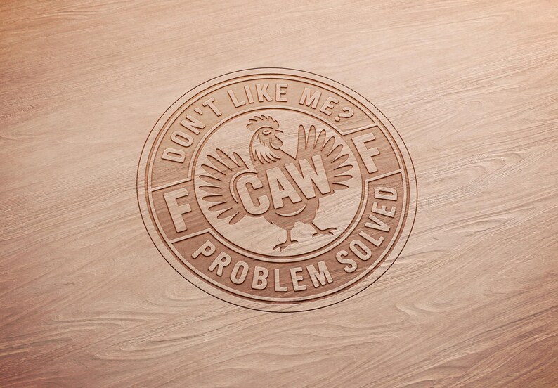 May include: A wooden circle with the text "DON'T LIKE ME? F CAW PROBLEM SOLVED" engraved around a rooster illustration. The rooster has outstretched wings and the word "CAW" in its body. The design is on a light brown wood surface.