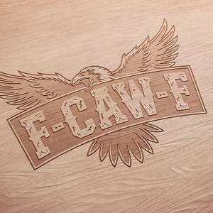 May include: A wooden carving featuring an eagle with outstretched wings and the text "F-CAW-F" on a banner. The design is etched into a light brown wooden surface, showcasing the grain.