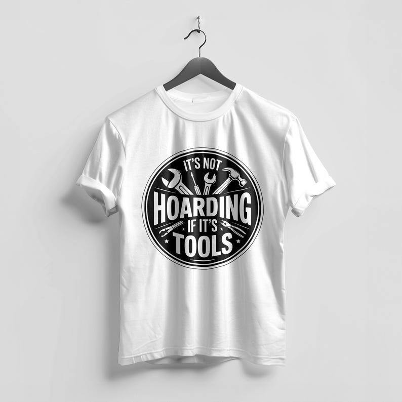 May include: White t-shirt with a black and white graphic. The graphic features tools like a wrench, hammer, and pliers inside a circular design. The text reads "IT'S NOT HOARDING IF IT'S TOOLS."