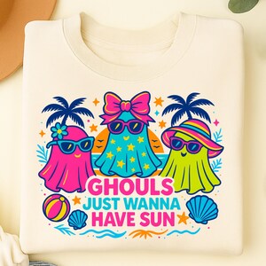 May include: Cream-colored sweatshirt featuring a colorful graphic of three cartoon ghosts wearing sunglasses and beach attire. The text "Ghouls Just Wanna Have Sun" is below the ghosts, with palm trees, stars, and beach ball accents.
