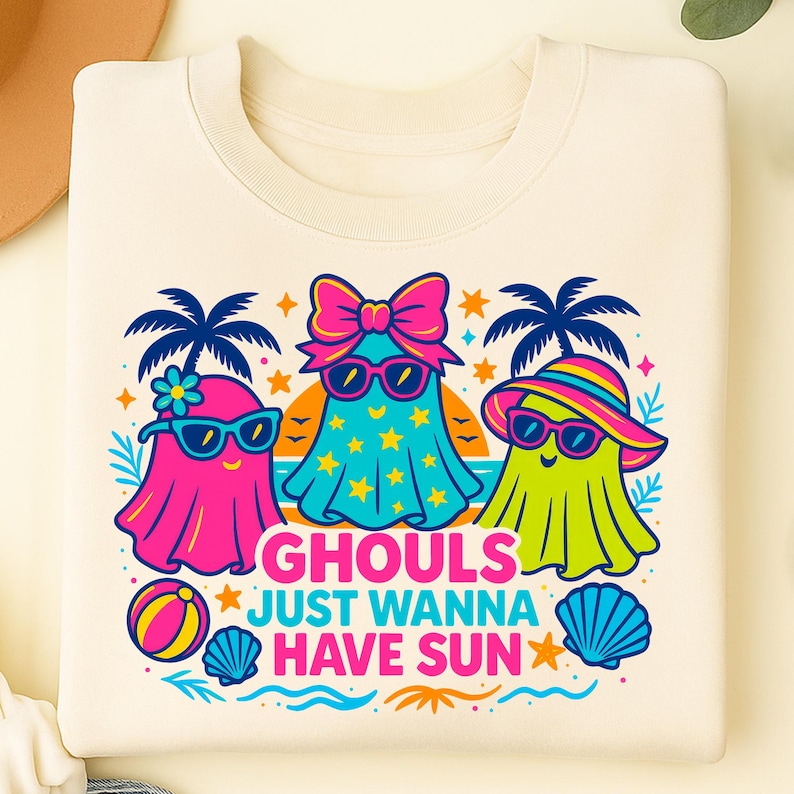 May include: Cream-colored sweatshirt featuring a colorful graphic of three cartoon ghosts wearing sunglasses and beach attire. The text "Ghouls Just Wanna Have Sun" is below the ghosts, with palm trees, stars, and beach ball accents.