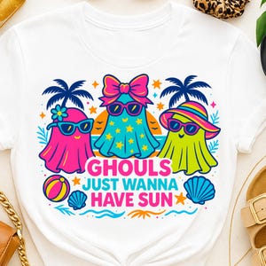 May include: White t-shirt featuring a colorful graphic of three cartoon ghosts wearing sunglasses and beach attire. The text "Ghouls Just Wanna Have Sun" is displayed below the ghosts, with beach-themed illustrations.