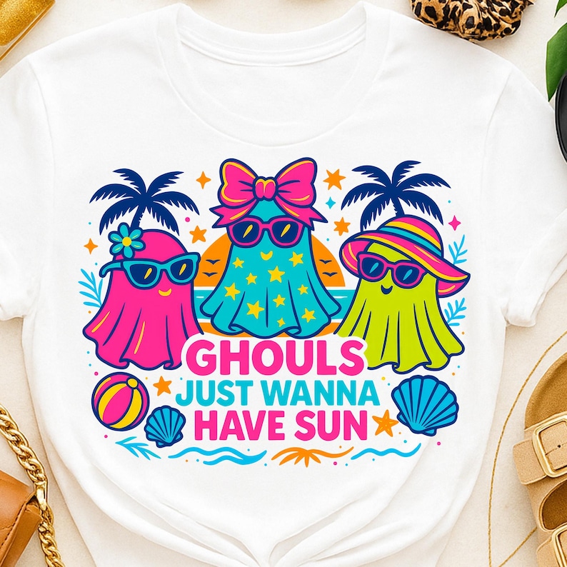 May include: White t-shirt featuring a colorful graphic of three cartoon ghosts wearing sunglasses and beach attire. The text "Ghouls Just Wanna Have Sun" is displayed below the ghosts, with beach-themed illustrations.