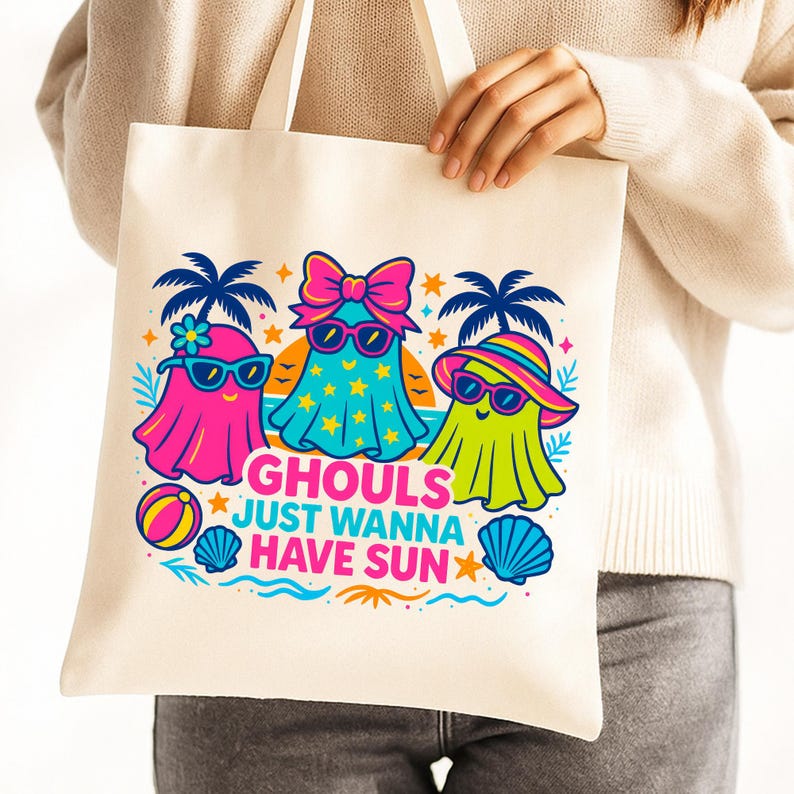 May include: A cream-colored tote bag featuring a colorful graphic of three ghost characters wearing sunglasses and beach attire. The text "Ghouls Just Wanna Have Sun" is printed below the ghosts, with palm trees and beach elements.