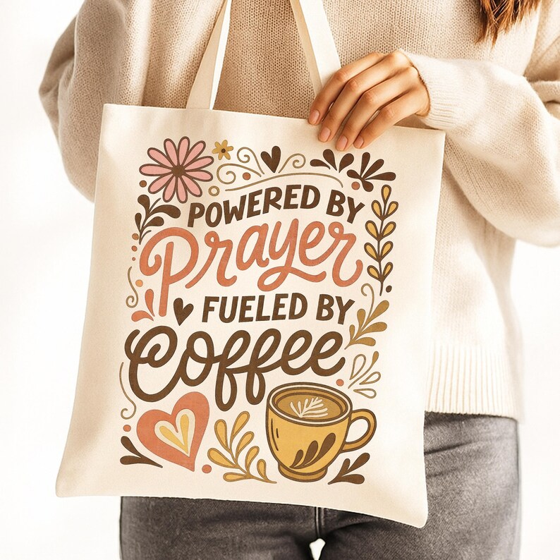May include: Cream-colored tote bag with the text "Powered by Prayer Fueled by Coffee." The design includes floral and heart motifs, and a coffee cup illustration. The bag has cream-colored handles.