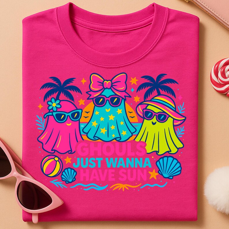 May include: A hot pink t-shirt featuring a graphic of three cartoon ghosts wearing sunglasses and beach attire. The ghosts are in shades of pink, blue, and yellow. Text on the shirt reads "Ghouls Just Wanna Have Sun."