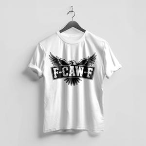 May include: White t-shirt with a black and white graphic. The graphic features an eagle with outstretched wings above a rectangular banner with the text "F-CAW-F". The shirt is hanging on a black hanger.