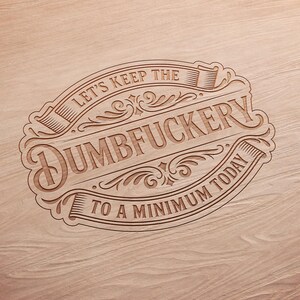 Puede incluir: Un letrero de madera con la frase "LET'S KEEP THE DUMBFUCKERTY TO A MINIMUM TODAY" en un dise&ntilde;o decorativo de estilo vintage. El texto est&aacute; tallado en la madera, con un color marr&oacute;n claro.