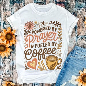 May include: White t-shirt with the text "POWERED BY PRAYER FUELED BY COFFEE" in brown, orange, and peach colors. The design includes a coffee cup, hearts, and floral elements. The shirt is paired with blue denim shorts.