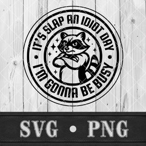 May include: Black and white graphic of a raccoon with crossed arms inside a circular design. Text around the raccoon reads "It's Slap an Idiot Day, I'm Gonna Be Busy." Below the circle are the letters "SVG" and "PNG".
