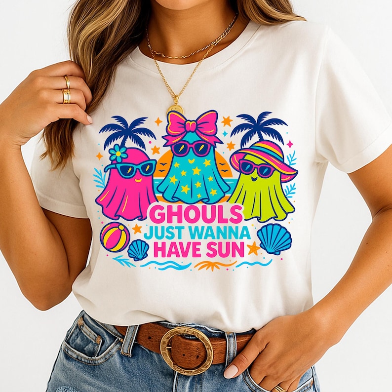 May include: White t-shirt featuring a colorful graphic of three cartoon ghosts wearing sunglasses and beach attire. The text "GHOULS JUST WANNA HAVE SUN" is below the ghosts. The design includes palm trees, stars, a beach ball, and a seashell.
