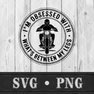 May include: Black and white graphic design featuring a motorcycle rider inside a circular frame. The text reads "I'M OBSESSED WITH WHAT'S BETWEEN MY LEGS." Below the graphic are the letters "SVG • PNG". The background is a light wood pattern.