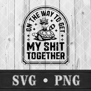 May include: Black and white graphic design featuring a raccoon wearing a hat, sitting on a turtle. The text reads "ON THE WAY TO GET MY SHIT TOGETHER". Below the graphic are the letters "SVG" and "PNG".