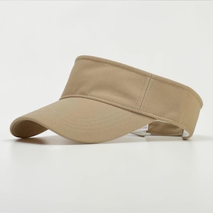 May include: A beige visor hat with a curved peak. The hat is made of a plain, neutral-coloured fabric. The visor is designed to protect the eyes from the sun. A classic accessory for outdoor activities.