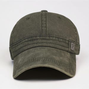 Puede incluir: Gorra de b&eacute;isbol verde oliva desgastada con visera curva. La gorra presenta un peque&ntilde;o emblema met&aacute;lico en el lateral y detalles de costura visibles. Aspecto vintage.