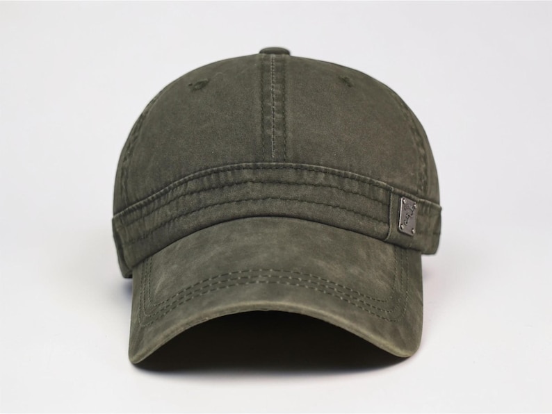 Puede incluir: Gorra de b&eacute;isbol verde oliva desgastada con visera curva. La gorra presenta un peque&ntilde;o emblema met&aacute;lico en el lateral y detalles de costura visibles. Aspecto vintage.