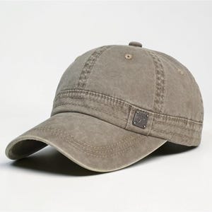 Puede incluir: Gorra de b&eacute;isbol verde oliva desgastada con visera curva. La gorra presenta un peque&ntilde;o emblema cuadrado en el lateral y detalles de costura visibles. El sombrero est&aacute; hecho de tela duradera y tiene un aspecto ligeramente descolorido.
