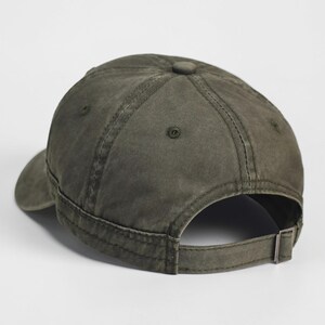 Puede incluir: Gorra de b&eacute;isbol verde oliva con visera curva y correa ajustable. La gorra tiene un dise&ntilde;o cl&aacute;sico de seis paneles con un bot&oacute;n en la parte superior y un cierre de hebilla met&aacute;lica en la parte posterior. La tela parece algod&oacute;n lavado y desgastado.