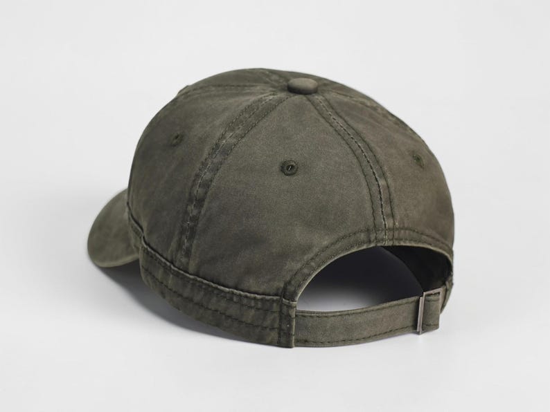 Puede incluir: Gorra de b&eacute;isbol verde oliva con visera curva y correa ajustable. La gorra tiene un dise&ntilde;o cl&aacute;sico de seis paneles con un bot&oacute;n en la parte superior y un cierre de hebilla met&aacute;lica en la parte posterior. La tela parece algod&oacute;n lavado y desgastado.