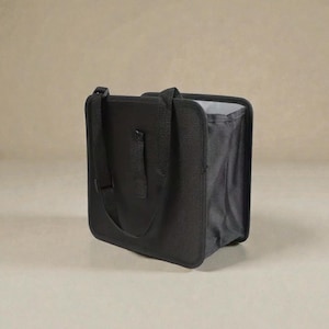 Könnte beinhalten: Eine schwarze Tragetasche mit rechteckiger Form und einem Griff oben. Die Tasche hat einen Schultergurt und ein graues Innenfutter. Die Tasche ist aus strapazierfähigem Material gefertigt und zum Tragen von Gegenständen bestimmt.