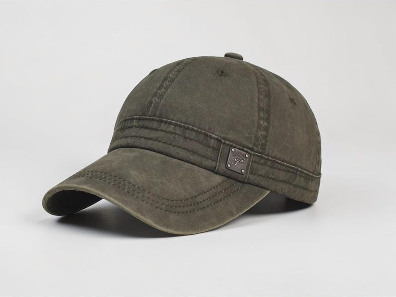 Puede incluir: Gorra de b&eacute;isbol verde oliva con visera curva. La gorra presenta un peque&ntilde;o parche rectangular en el lateral. El sombrero tiene un aspecto ligeramente desgastado, con detalles de costura visibles. La gorra es de color liso y tiene un bot&oacute;n en la parte superior.