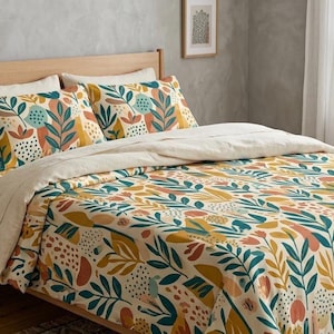 May include: A bed featuring a duvet cover and pillowcases with a multi-colored botanical pattern in shades of mustard yellow, teal, and coral on a cream background. A solid cream-colored flat sheet is folded over the top, and a light blue throw blanket.