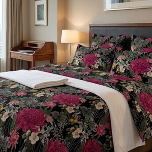 May include: A bed featuring a black duvet cover and matching pillowcases decorated with a vibrant floral pattern of large magenta chrysanthemums and smaller white and yellow flowers, topped with a folded white blanket against a dark headboard.