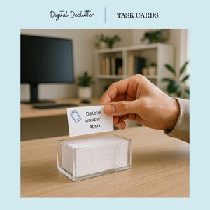 May include: A clear acrylic task card holder filled with white cards. One card is being held up, displaying a smartphone icon and the text "Delete unused apps." The words "Digital Declutter" and "TASK CARDS" are at the top.