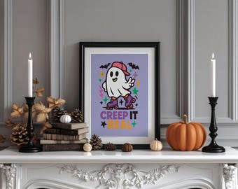 以下が含まれることがあります： 赤い帽子とローラースケートを履いた漫画の幽霊が描かれた、ハロウィーンをテーマにした額入りのプリント。テキストは「Creep It Real」です。プリントは、ろうそく、カボチャ、装飾要素のある白いマントルピースに表示されています。