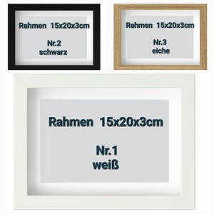 May include: Three framed art pieces. The top left frame is black, the top right is light brown, and the bottom frame is white. Each frame has a white mat and a printed label with text. The text on each label reads "Rahmen 15x20x3cm".