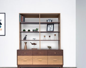 May include: A mid-century modern style wooden bookcase and dresser with four drawers. The bookcase has five shelves and is filled with decorative items, including a framed print, a camera, and plants. The dresser has a walnut finish and is made of wood.