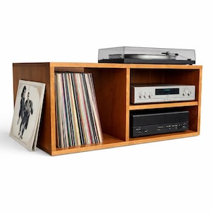 May include: A wooden media console with a turntable, stereo receiver, and a black component. The console has compartments for vinyl records and album art. The unit is made of light brown wood.