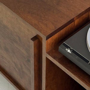 May include: A dark brown wooden record player stand with a record player on top. The stand has a shelf and a small compartment.