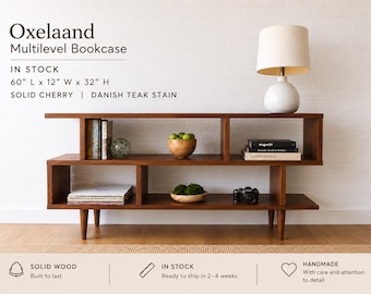 Può includere: Libreria a più livelli Oxelaand, 152,4 cm di lunghezza, 30,5 cm di larghezza e 81,3 cm di altezza, realizzata in legno di ciliegio massello con tinta teak danese. Questo scaffale rettangolare basso in legno ha quattro gambe affusolate.